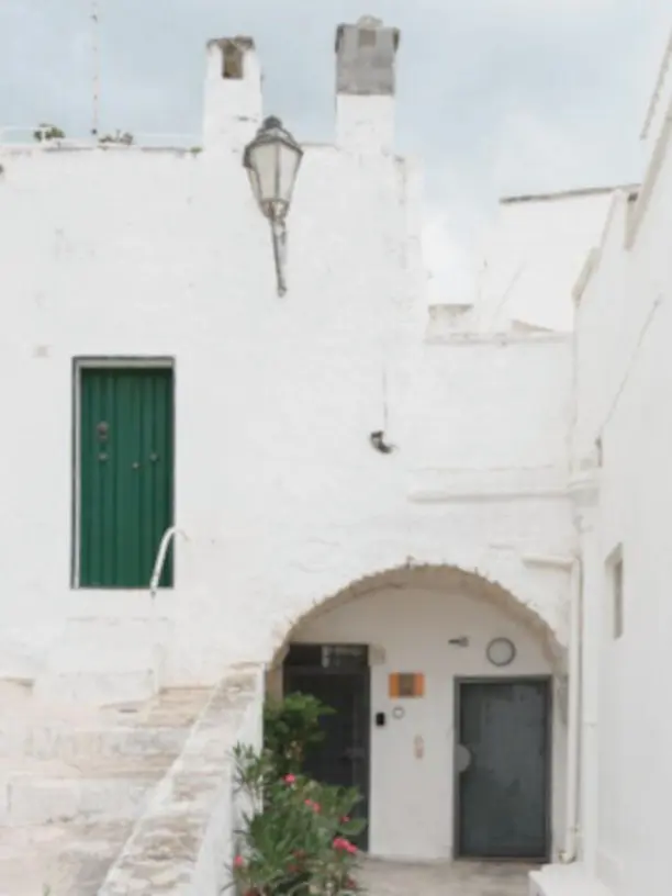 Facciata bianca con arco in pietra e porta verde del B&B Atagio nel centro storico di Ostuni, tipica architettura pugliese